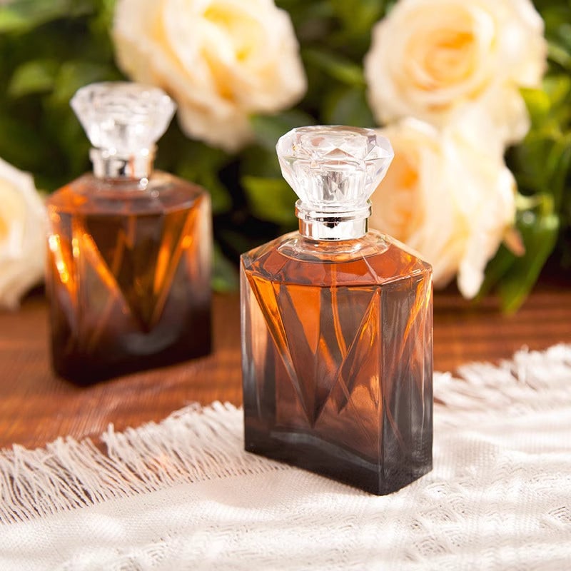 Faceted amber glass perfume bottles beside cream roses on a fringed cloth